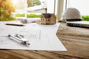 Plan d'architecte, maquette de maison et casque de chantier sur un bureau